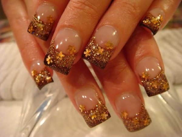 Ongles unis avec des pointes brunes et des fleurs oranges et des décorations scintillantes