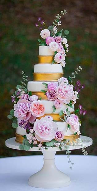Πολυτελές λευκό και χρυσό κέικ με απαλά λουλούδια για καλοκαιρινές γαμήλιες τούρτες