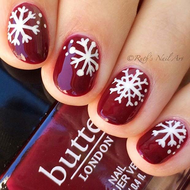 Ongles rouge foncé avec des flocons de neige blancs