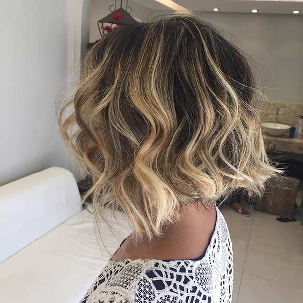 Coupe de cheveux ondulée foncée et courte avec des reflets de balayage blond miel