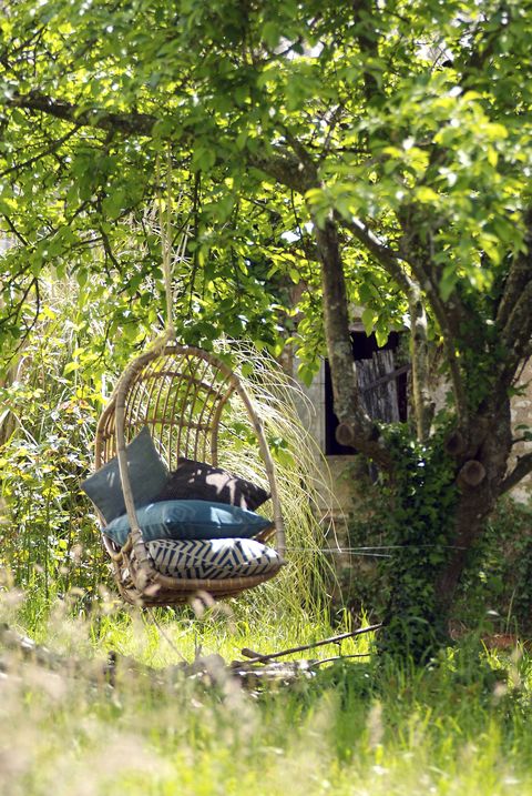 balançoire de jardin entourée de feuillage vert avec une pile de coussins