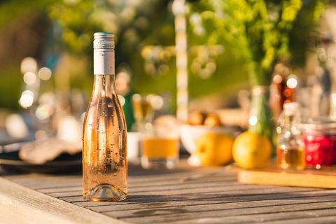 בקבוק יין רוזה קר שלא נפתח על שולחן ארוחת ערב באמצע הקיץ בשבדיה מתמקד בבקבוק הטפטוף בחזית