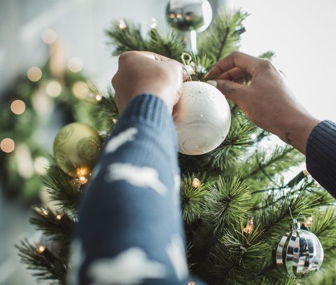 νεαρός άνδρας που γιορτάζει τα Χριστούγεννα στο σπίτι και διακοσμεί το σπίτι του χριστουγεννιάτικου δέντρου είναι διακοσμημένος με χριστουγεννιάτικα στολίδια και φώτα