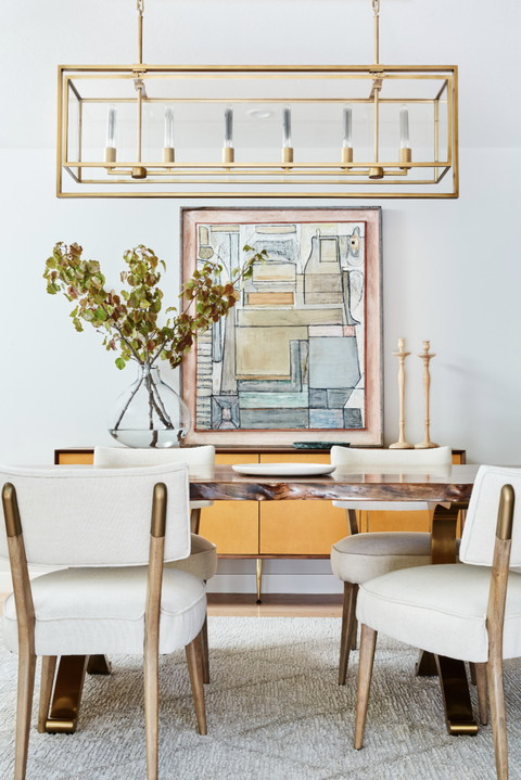 détails de la salle à manger avec lustre en or linéaire, table en bois et meubles d'armoire jaune et marron