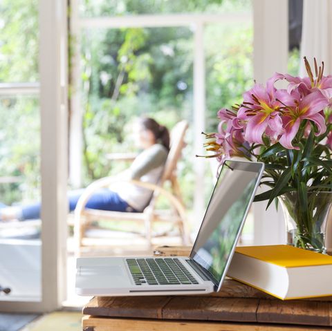 salon décoré de fleurs avec livre et ordinateur portable femme relaxante à l'extérieur sur une terrasse