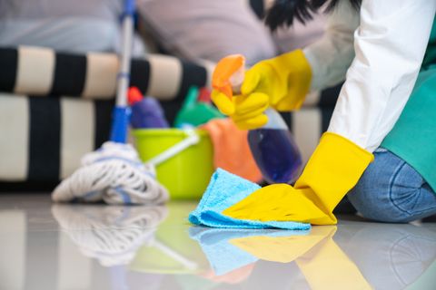 concept de ménage et de nettoyage de mari, jeune femme heureuse dans des gants en caoutchouc bleu essuyant la poussière à l'aide d'un spray et d'un plumeau tout en nettoyant le sol à la maison