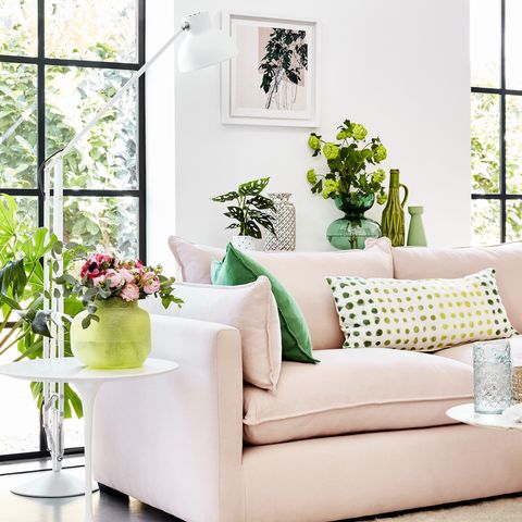 ספה ורודה בחדר לבן עם צמחים ירוקים מסביב וכריות בדוגמת ירוק