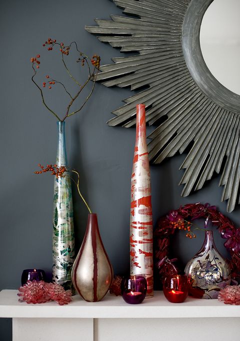 vases en verre rouge et bleu avec arrangement de brindilles, bougeoirs, cheminée, miroir rayon de soleil, couronne de noël, festif, contre mur gris