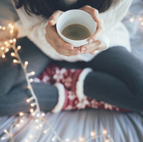 femme assise à la maison les jambes croisées sur le lit, tenant une tasse de café, décoration de noël