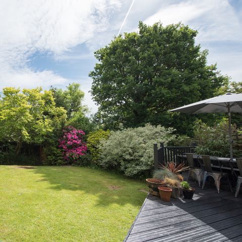 une vue générale d'un jardin arrière avec une terrasse grise avec table et chaises de jardin par une journée ensoleillée dans une maison