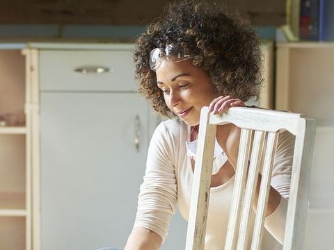 une femme restaure et améliore une vieille chaise en bois dans son atelier