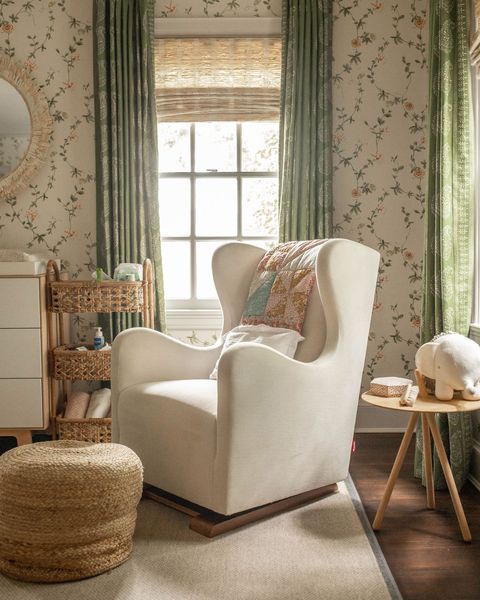חדר ילדים, כיסא נדנדה לבן עם שמיכת ורוד וכחול, שטיח באזור עירום ואפור, רצפת עץ, טפטים פרחוניים ווילונות ירוקים
